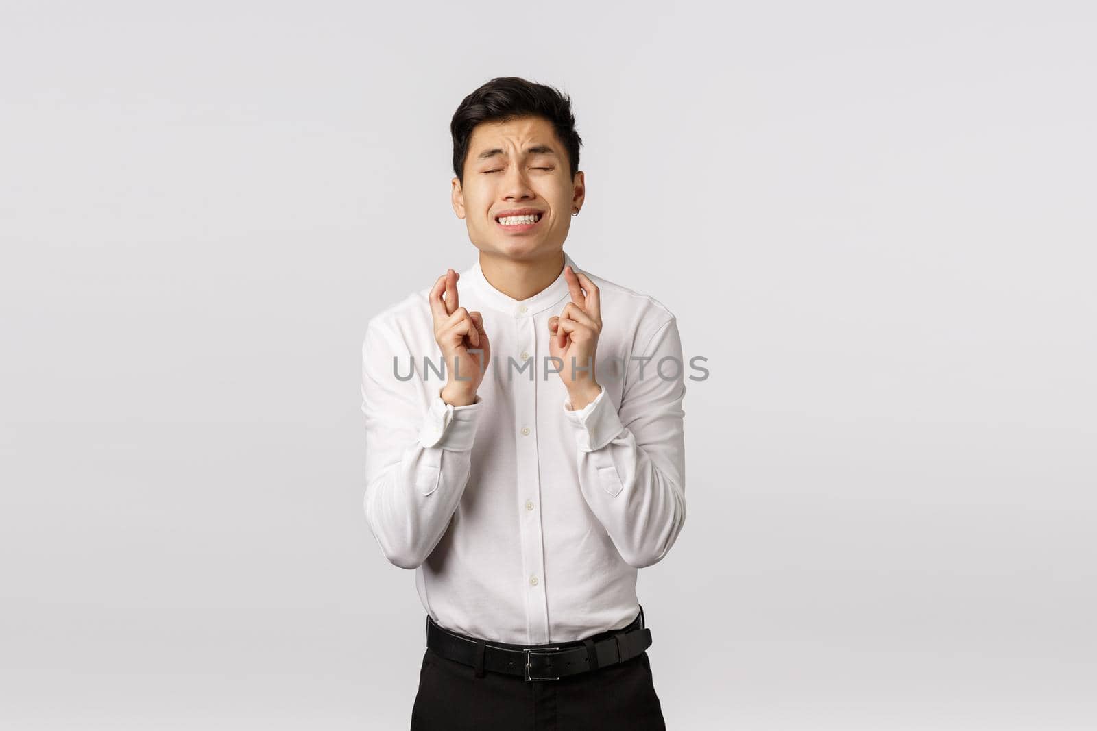 Worried, hopeful and alarmed young asian boyfriend praying god, asking grace or wish come true, close eyes cross fingers good luck, dream relish something, sign big deal, white background.