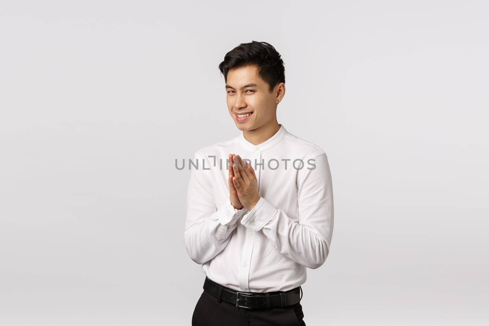 Hideous, sly handsome young asian male entrepreneur have something evil or genius in mind, rub palms near chest, squinting mysterious and smirk, have perfect plan, standing white background.
