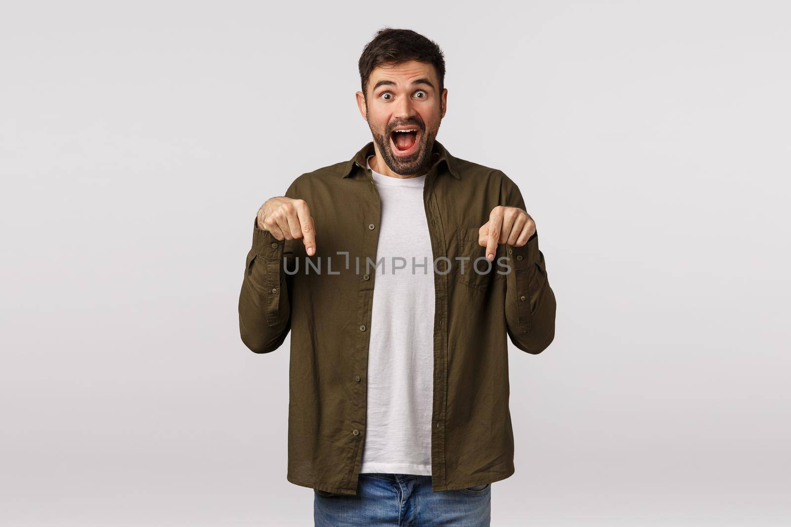 Man got invitation great event, sharing great news, bragging. Attractive bearded male in coat, pointing down and asking see, smiling joyfully, recommend product, web site for finding dream job by Benzoix