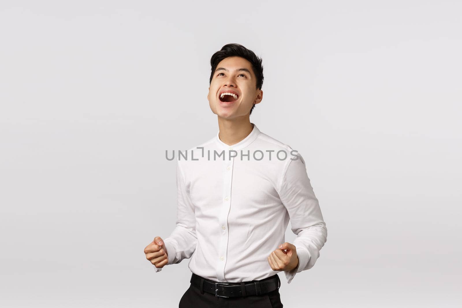 Yeah baby, thanks god I won. Man celebrating successful deal. Pleased, rejoicing attractive young asian guy fist pump, say yes at sky and smiling relieved, achieve goal, winning, white background by Benzoix