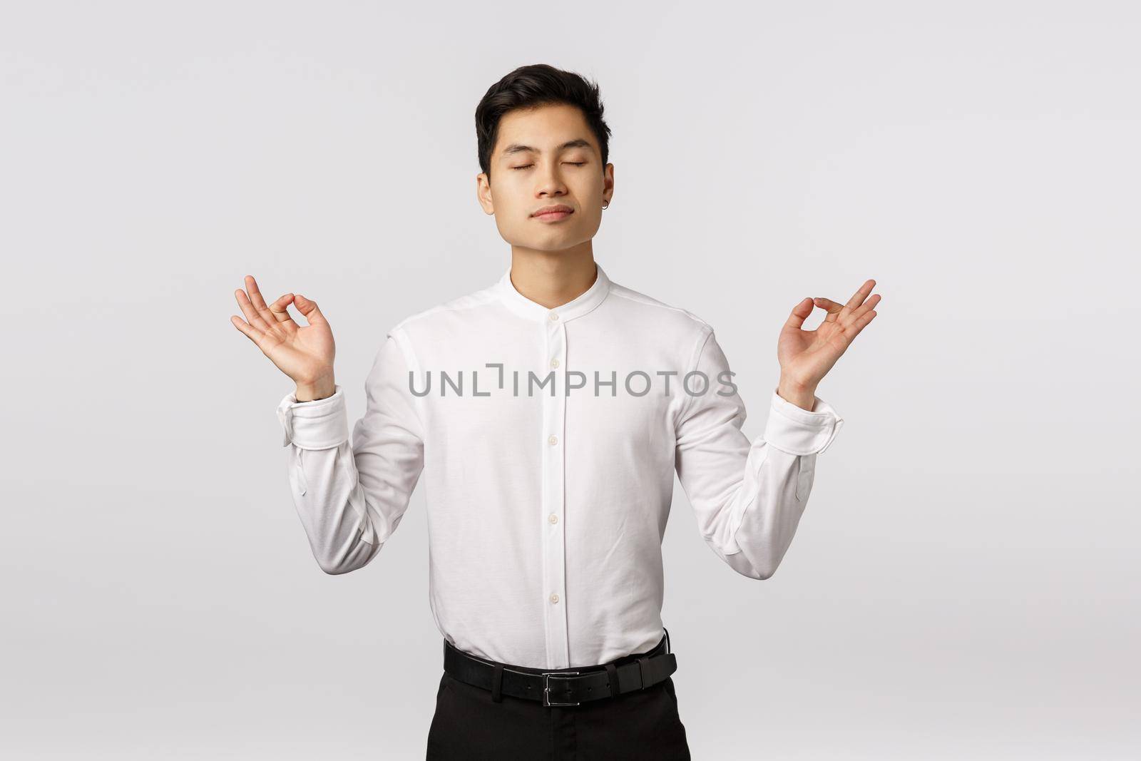 Peaceful and determined attractive asian businessman, calm down, release stress, close eyes and meditating in office, breathing practice with hands sideways, mudra or zen gesture, do yoga by Benzoix