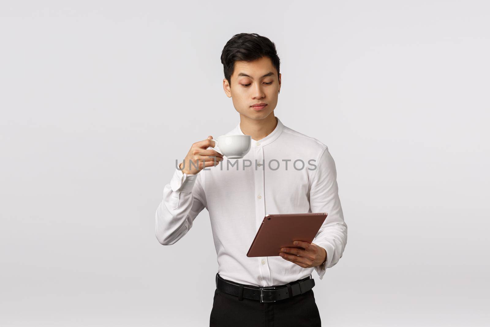 Business, technology and finance concept. Serious-looking elegant and stylish, successful male entrepreneur reading news in digital tablet, drinking coffee from cup, studying documents online.