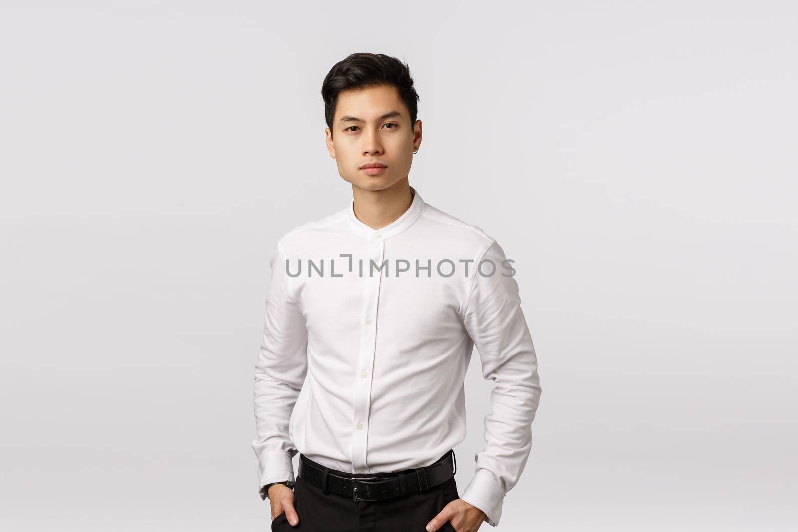 Serious-looking, determined successful wealthy asian businessman in white collar shirt, black pants, hold hands in pockets, looking camera, listening employee report about business, white background.