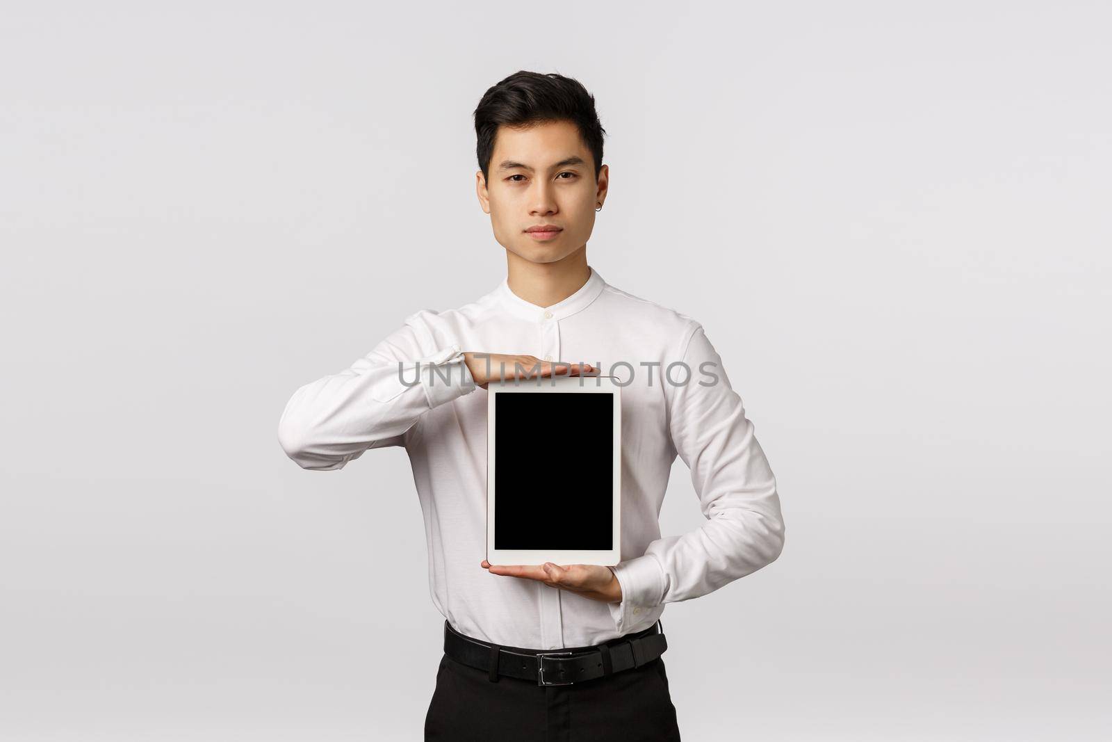 Guy knows exactly what you need. Serious-looking sassy and elegant asian man in formal outfit, holding digital tablet over chest, showing device screen, promote application or corporate link.