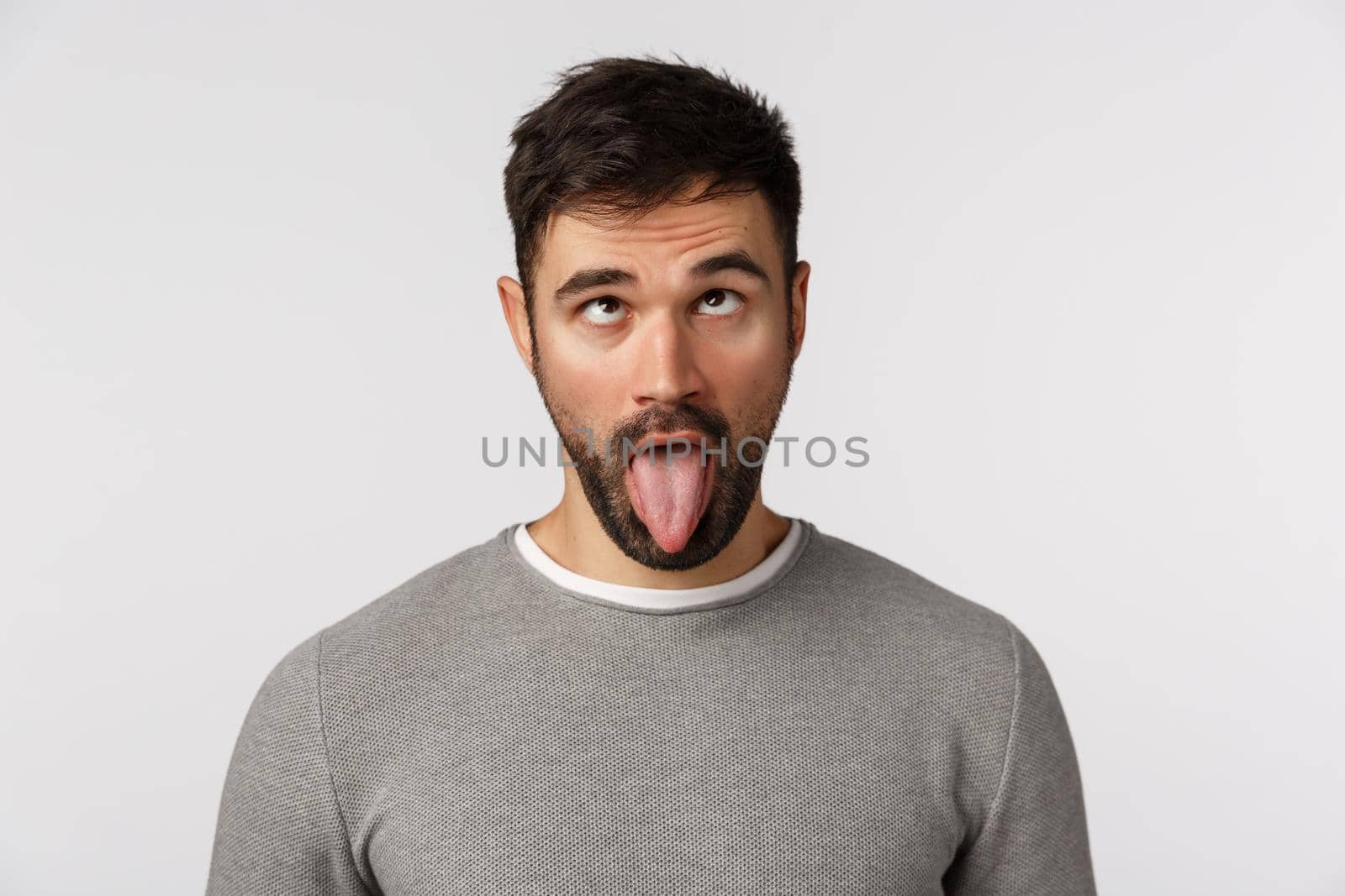 Close-up studio shot funny bearded guy going crazy home-sick home, showing tongue and roll eyelids upwards as making goofy, playful expression, standing white background stupid.