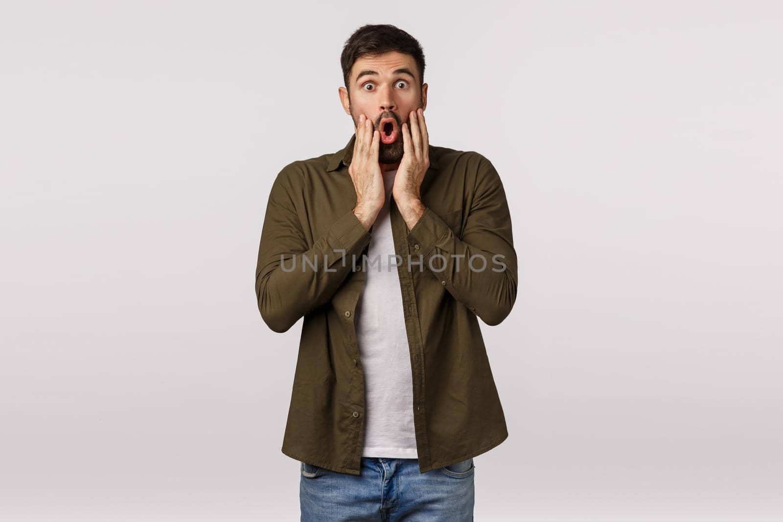 OMG check this out unbelievable. Astonished and speechless good-looking modern male in coat, lose breath, gasping amazed, say wow stare camera impressed, touch cheeks fascinated, white background.