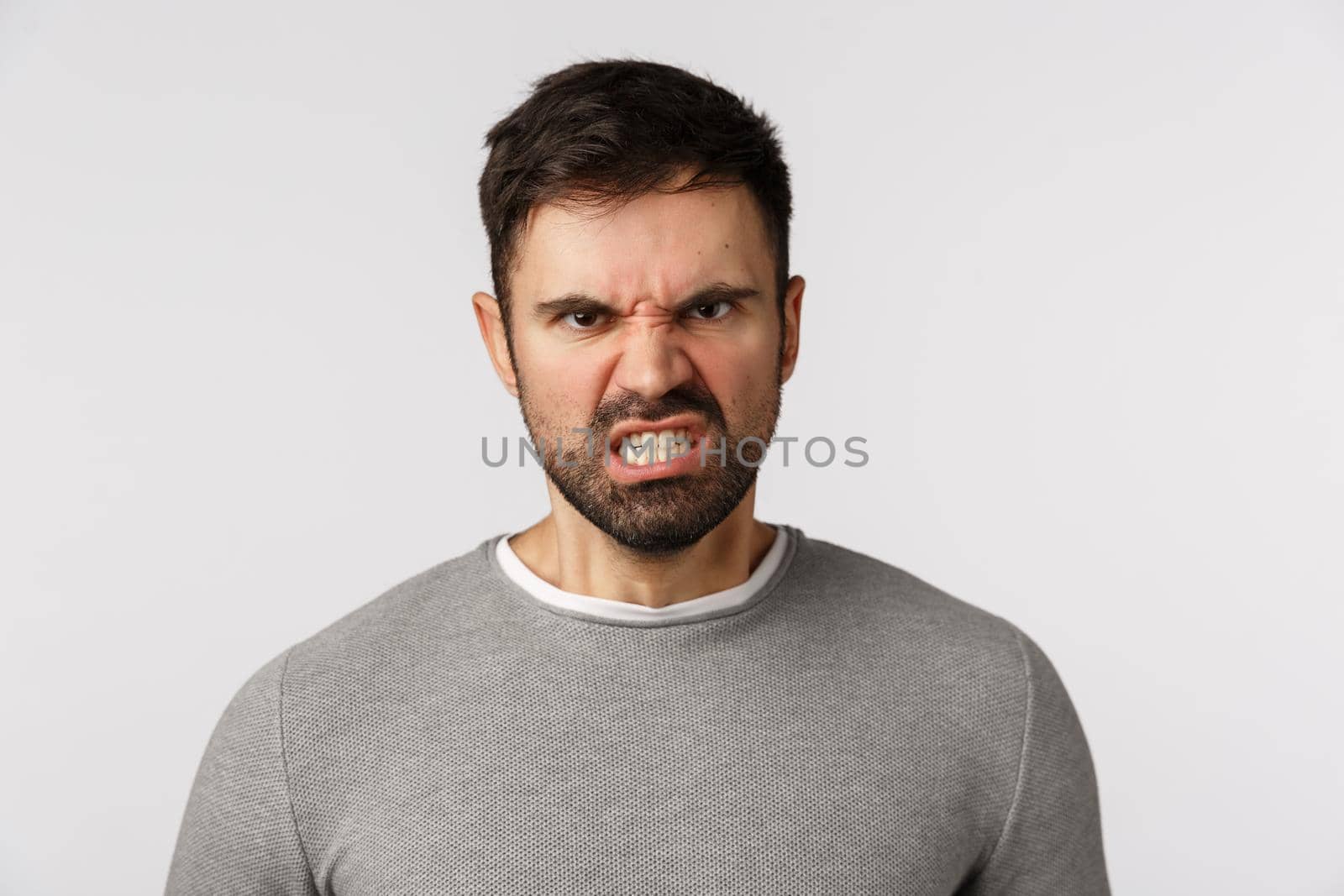 Hate, emotions and aggression concept. Hateful, furious caucasian bearded male in grey sweater, grimacing frowning look outrated and angry, grimacing clench fists, want punch enemy, white background.