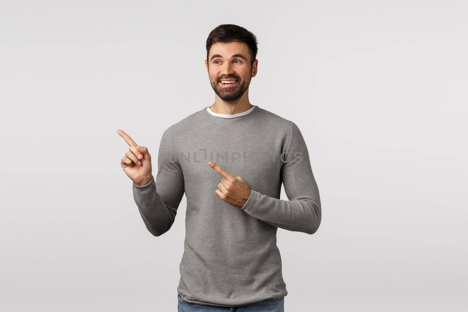 Pleased charming lucky young handsome male, adult in grey sweater, pointing looking left, observe cute scene, picked variant, see nice choice, happy and charmed, smiling satisfied.