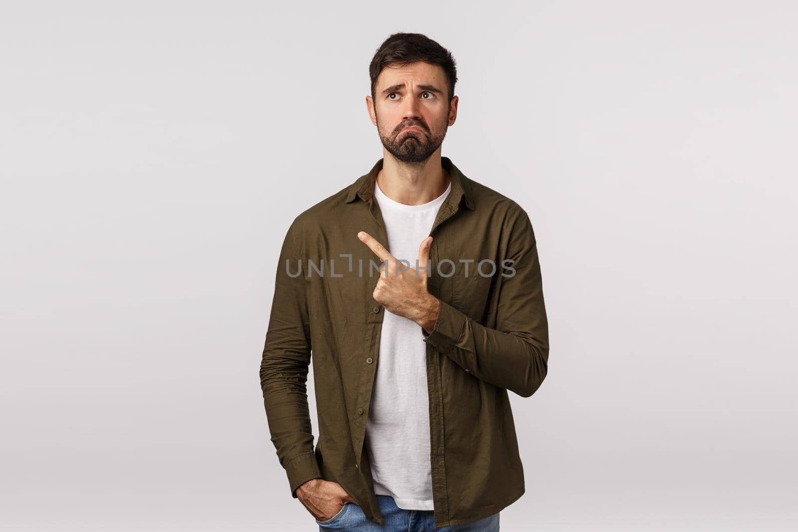 Man regret missed good opportunity feeling sad and miserable. Upset young bearded guy pulling gloomy face, frowning and look depressed, pointing upper left corner, standing white background.