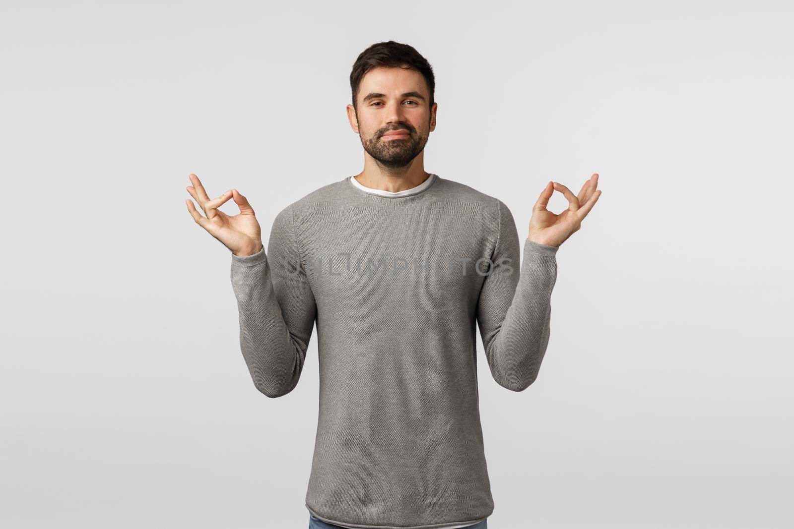 Peaceful and cheerful, smiling happy bearded male in grey sweater feeling okay after meditation, relief stress, hold hands sideways mudra, zen gesture, reach nirvana, practice yoga, white background.