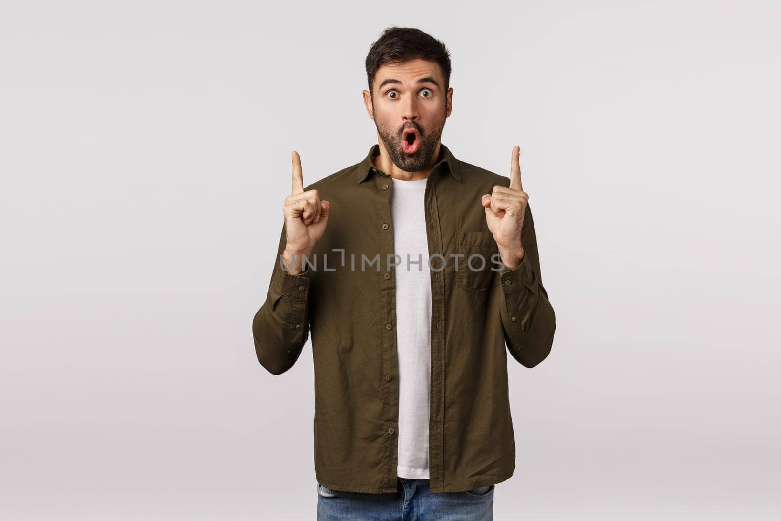 You must see this, wow. Amazed impressed and excited modern bearded male in coat, pointing up, folding lips thrilled, telling interesting news, showing friends great promo offer, discounts.