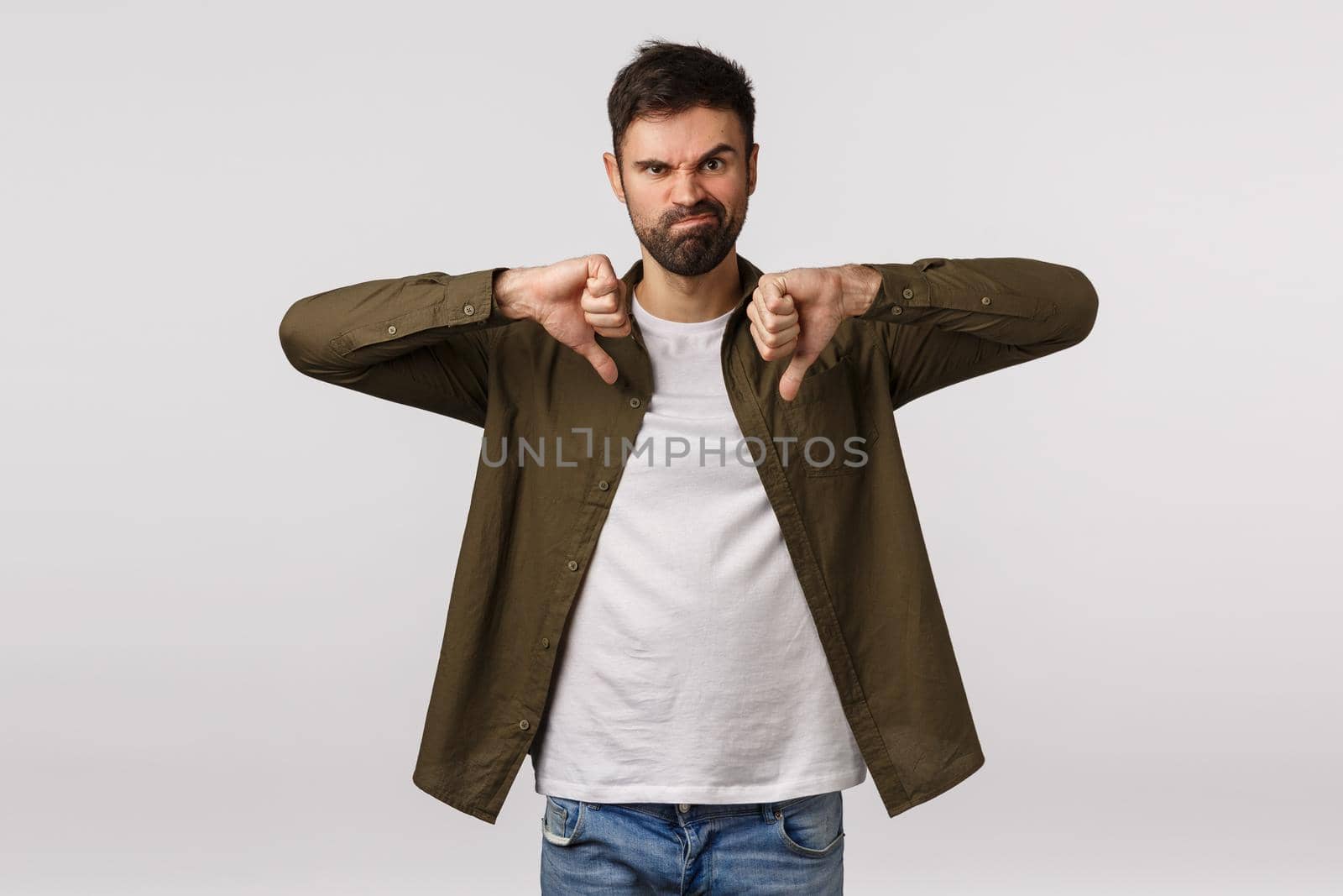 Wrong choice, totally dislike it. Displeased and unsatisfied male customer leave negative feedback, show thumbs-down, grimacing unhappy and disappointed, standing white background upset.