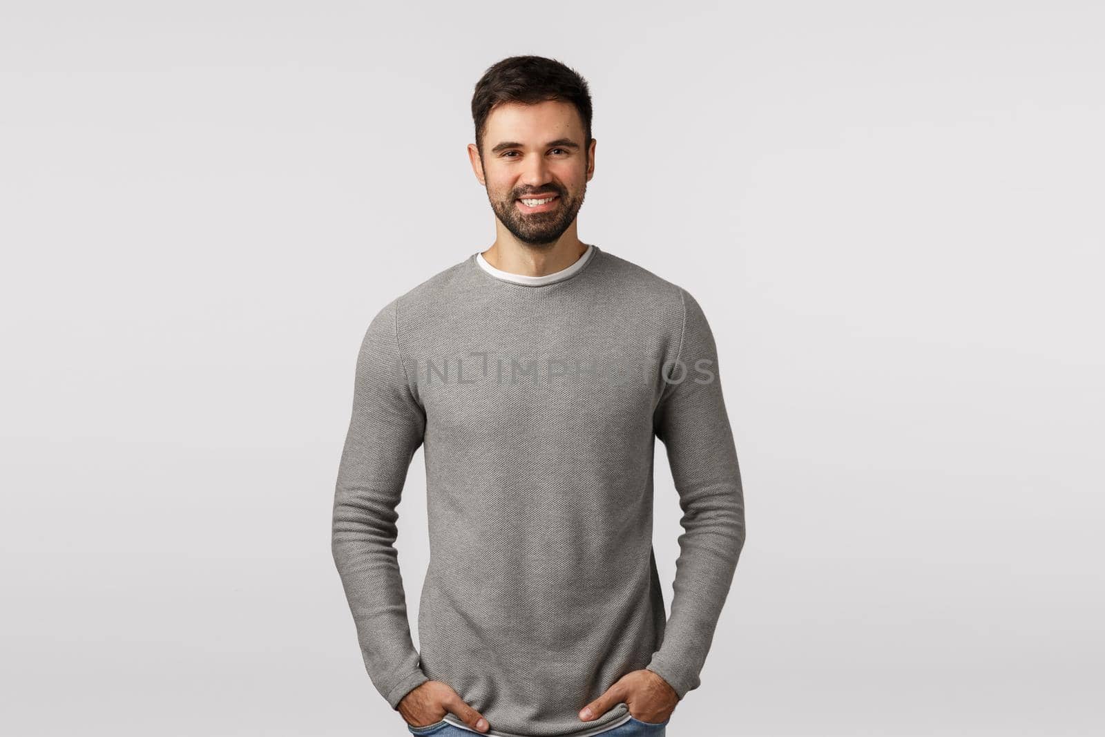 Cheerful, charismatic bearded, masculine guy in grey sweater, hold hands pockets, carefree pose, smiling delighted, speaking to client, discuss business, satisfied with good results, white background by Benzoix