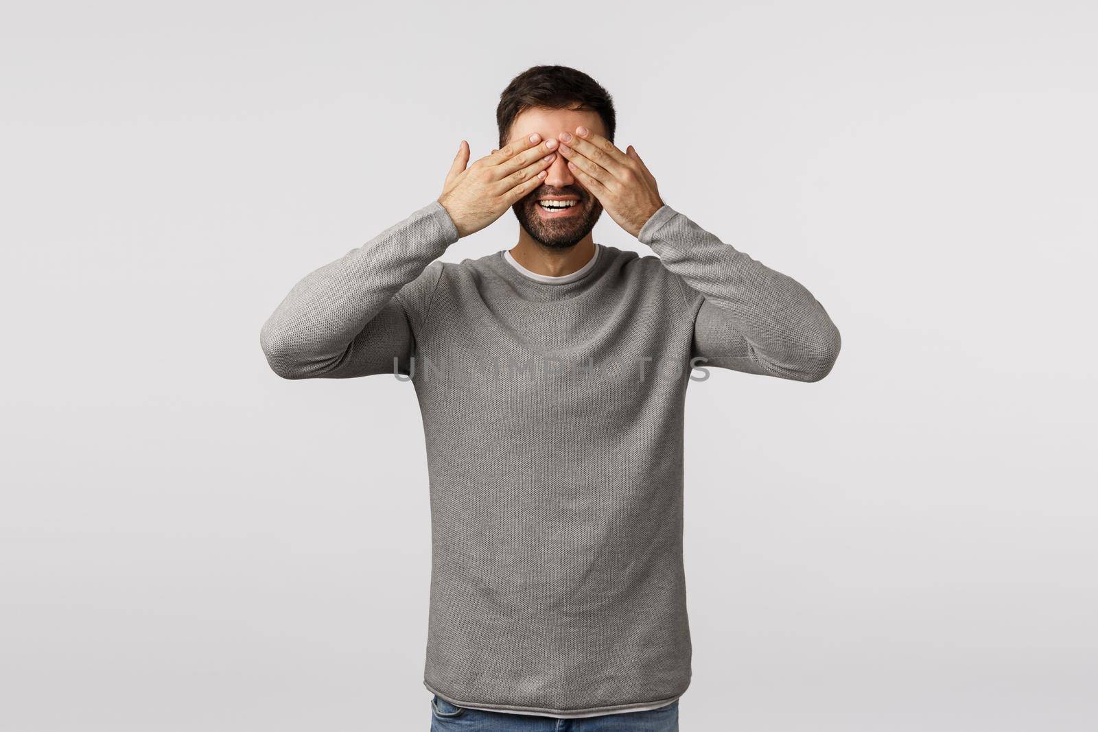 Peekabo, whos there. Cheerful and playful good-looking bearded young father playing baby hide n seek, close eyes standing blindfolded and smiling happy, standing white background waiting surprise.