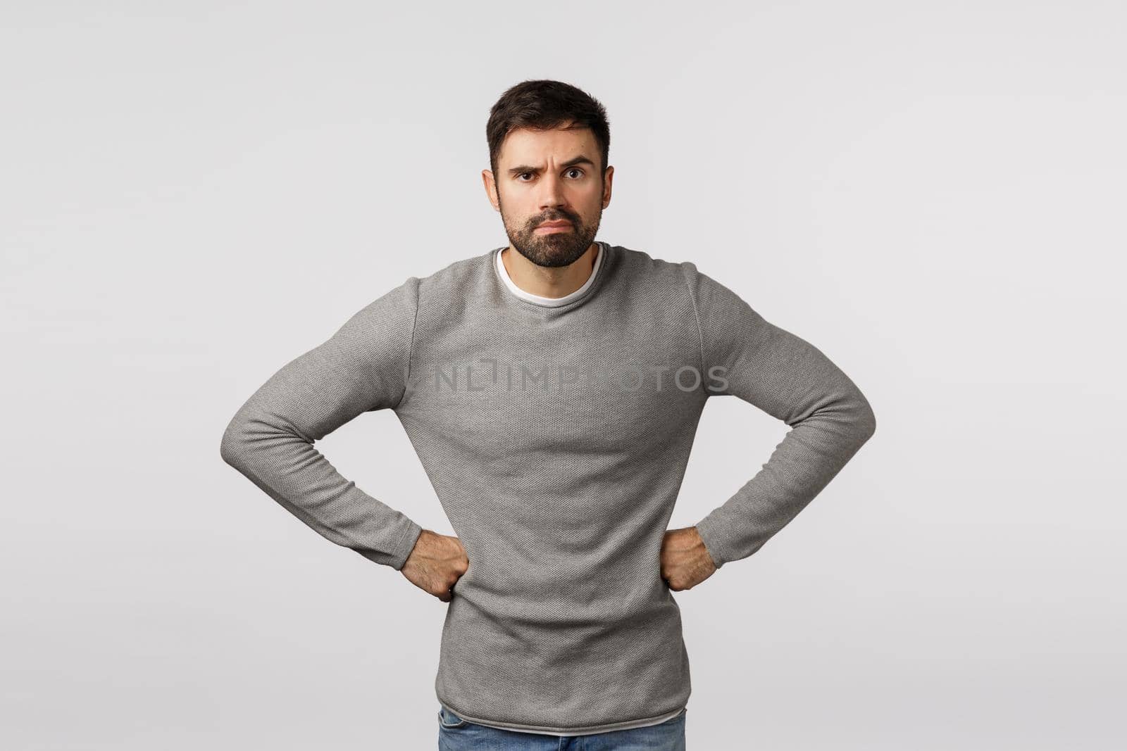 Angry and grumpy, displeased strict or serious male with beard, wear grey sweater, holding hands on waist in demanding, disappointed pose, frowning and grimacing upset, scolding someone by Benzoix