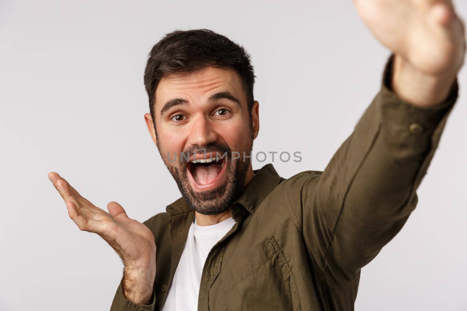 Happy and cheerful, glad young man introduce something as talking on online record video and describe product, hold smartphone extended arm, taking selfie, pointing left, white background by Benzoix