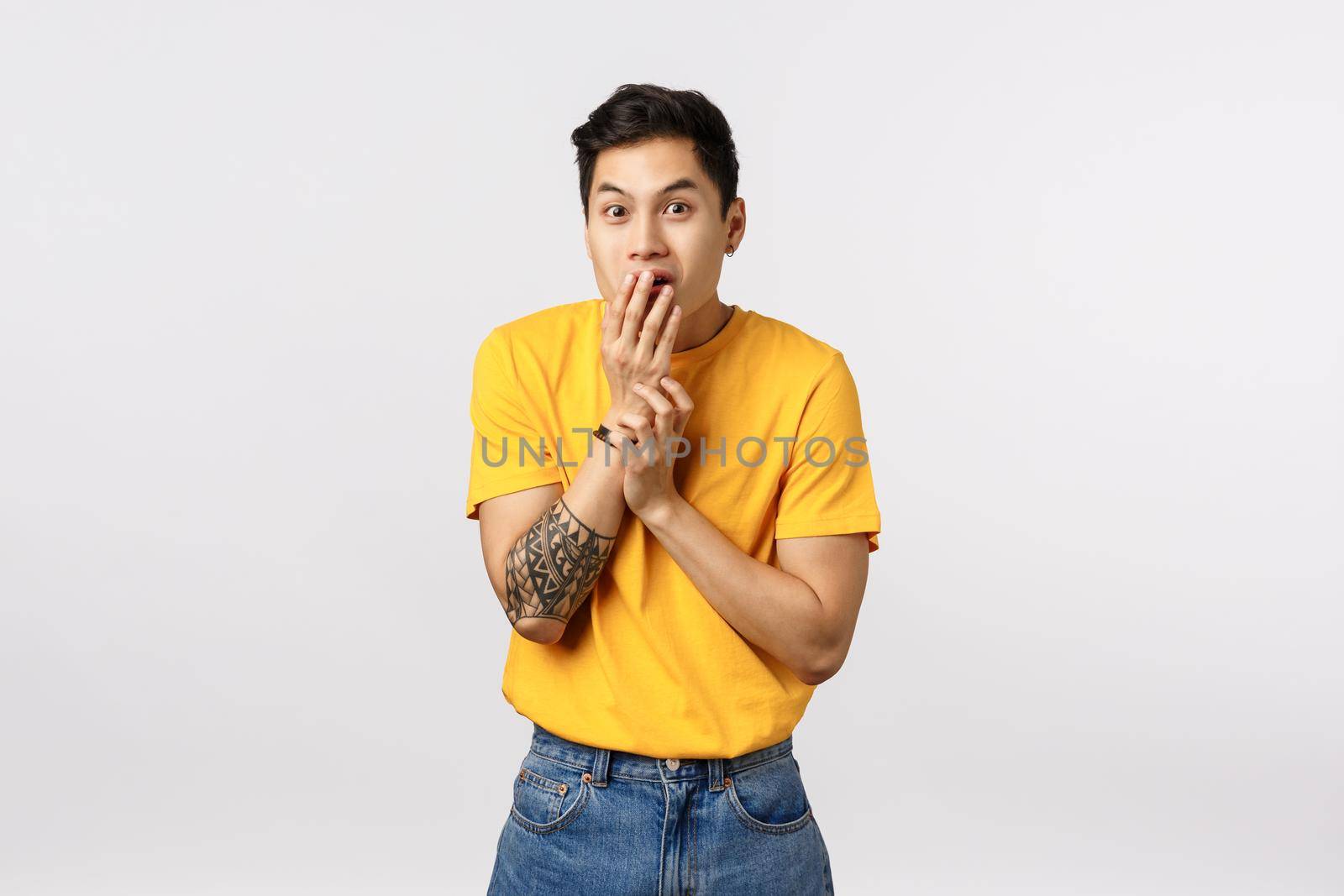 Wow no way, tell me more. Intrigued and excited handsome smiling asian guy with tattoos, cover mouth with palm, giggle and gasping surprised, gossiping, heard fresh rumor, white background.