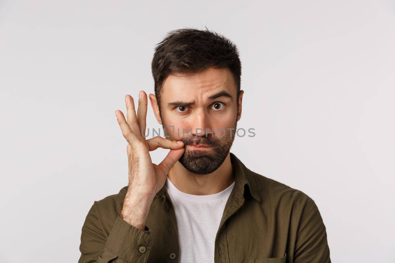 My lips are sealed with promise. Serious and funny bearded adult man keep mouth shut, making zip gesture and raise one eyebrow as hinting person stay silent, keep secret safe, white background.