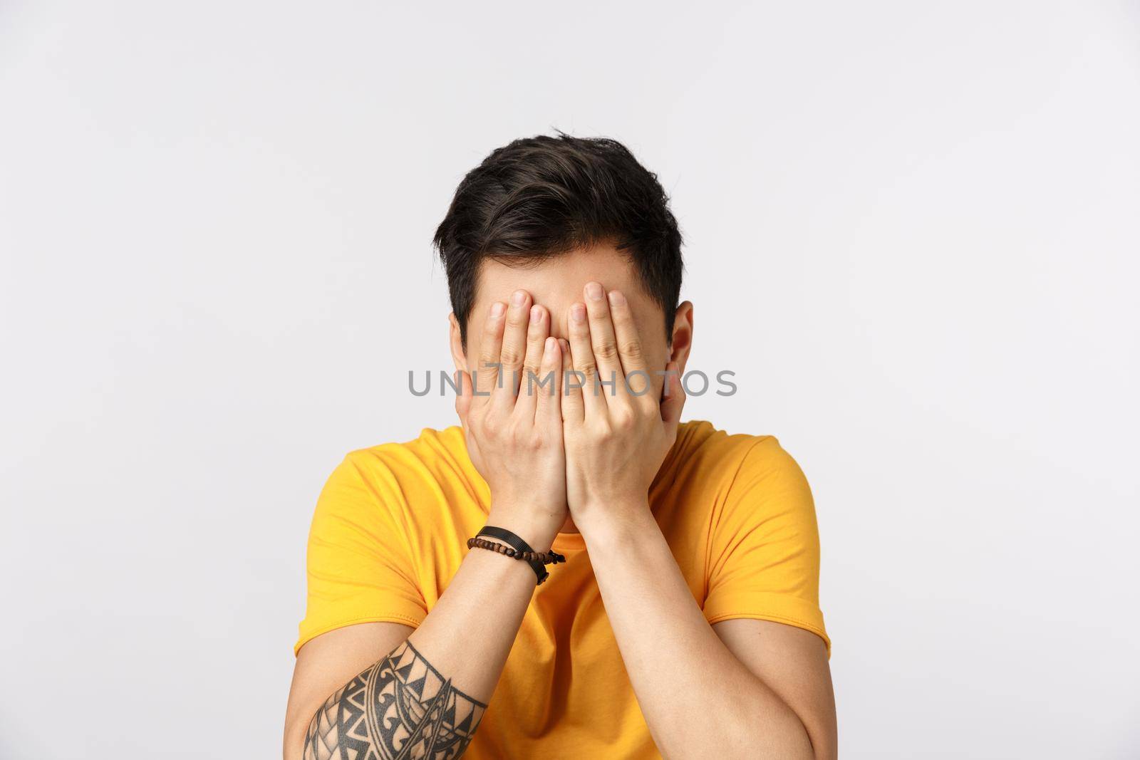 Scared young guy cover face with palms as dont want watch terrible scene in movie, standing white background afraid, express fright and insecurity, hiding eyes, standing white background blindfolded by Benzoix