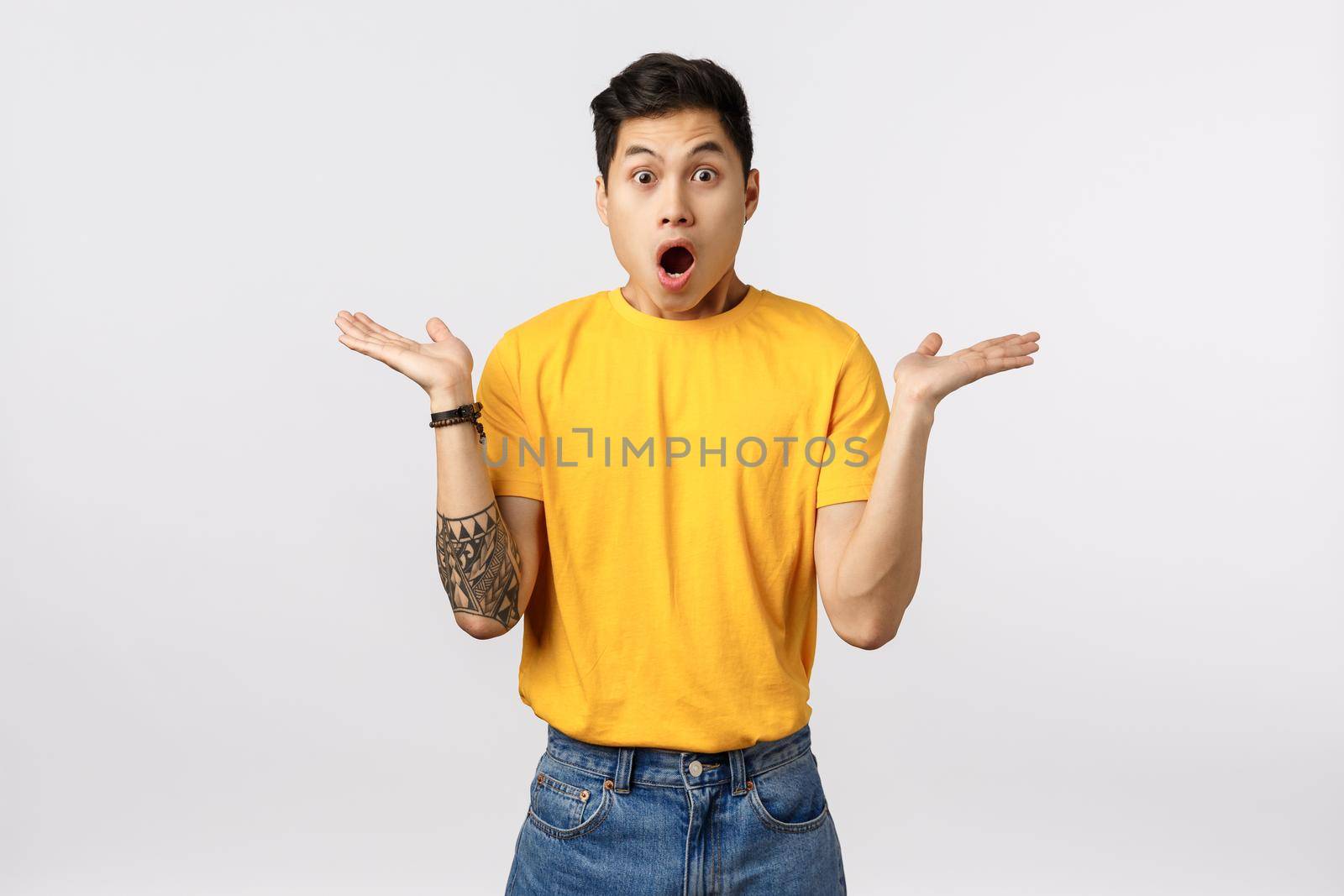 Shocked, impressed speechless asian young man in yellow t-shirt, spread ...