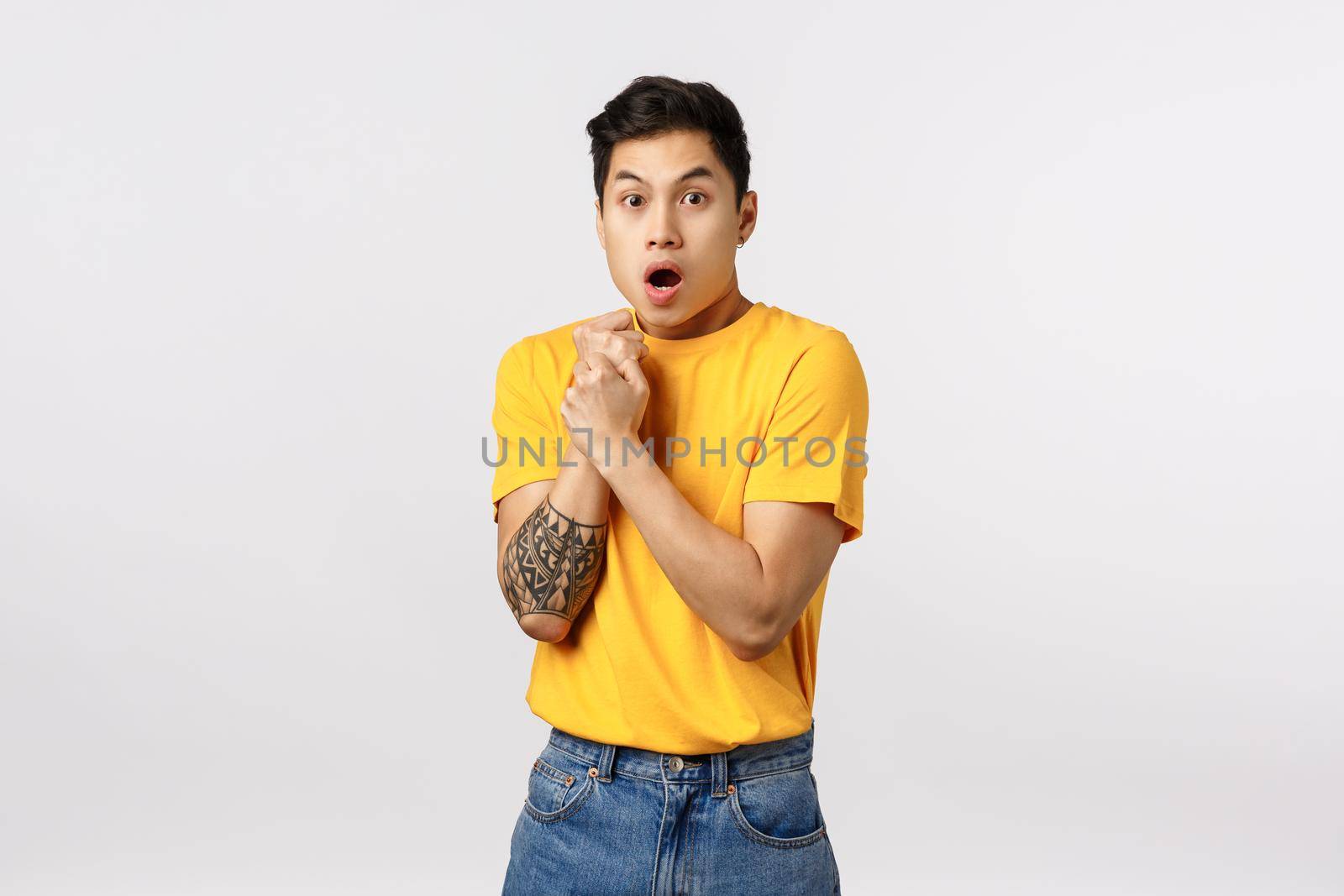 Sensetive and shocked, scared young asian guy with tattoos, pull hand back, press arm to chest insecure and afraid, gasping open mouth, look like victim at someone abuse him, stand white background.