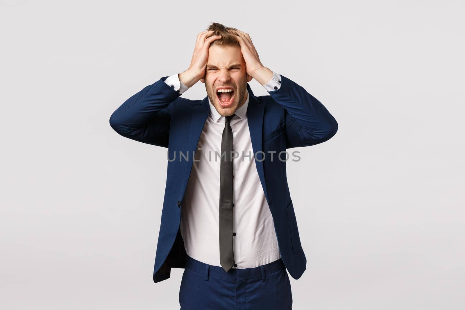 Distressed young businessman lost all money, feeling depressed and let down, frowning upset, screaming in rage, holding hands on head troubled, standing sad over white background. Copy space
