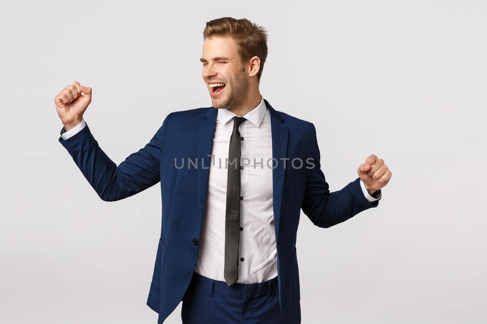 Success, entrepreneur and corporate concept. Attractive cheerful businessman in classic suit, raising hands up, fist pump and dancing celebrating, triumphing and smiling, achieve goal.