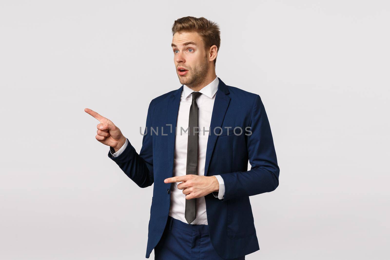 Surprised and speechless amazed businessman in classic suit, pointing staring left astonished, guy dressed up for meeting, christmas corporate party, checking out stunning product, white background.