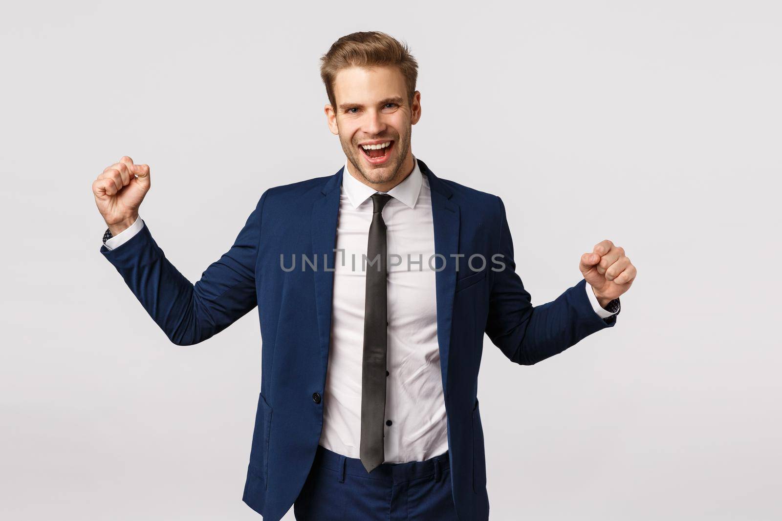 Relish, good deal and business concept. Handsome young blond bearded man in classic suit, businessman raising hands up, fist pump cheerful and smiling, celebrating, triumphing relish, made money.
