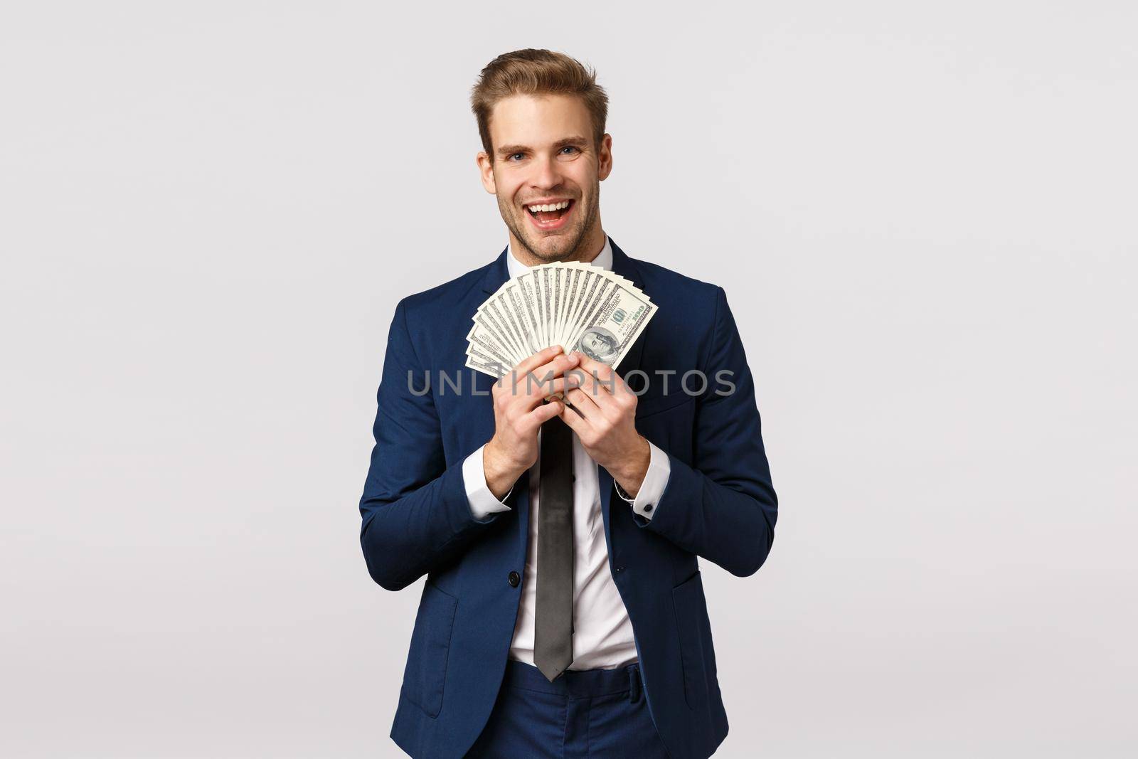 Guy bragging with money. Attractive blond bearded businessman in classic suit, holding lots cash, showing dollars and smiling satisfied, won lottery, sport bet, standing white background pleased by Benzoix