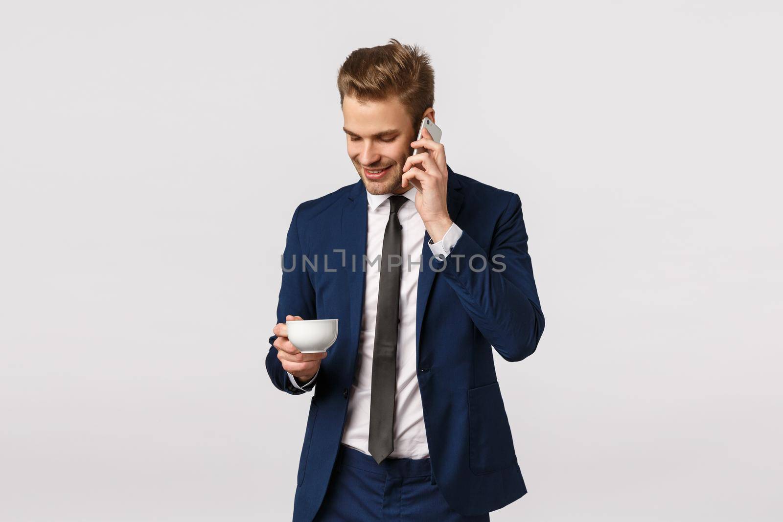 Office, corporate and business concept. Confident, good-looking elegant male entrepreneur starting own business deal with partners over phone, holding smartphone, calling friend, drink coffee by Benzoix