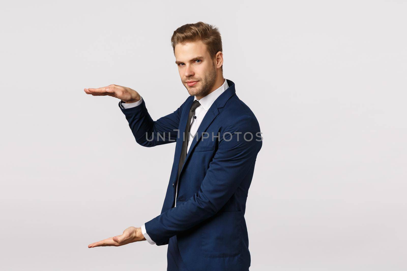 Man showing something big. Attractive bearded blond businessman in classic suit, hold hand as holding something, shaping large object, diagram, showing amount money can gain, white background.