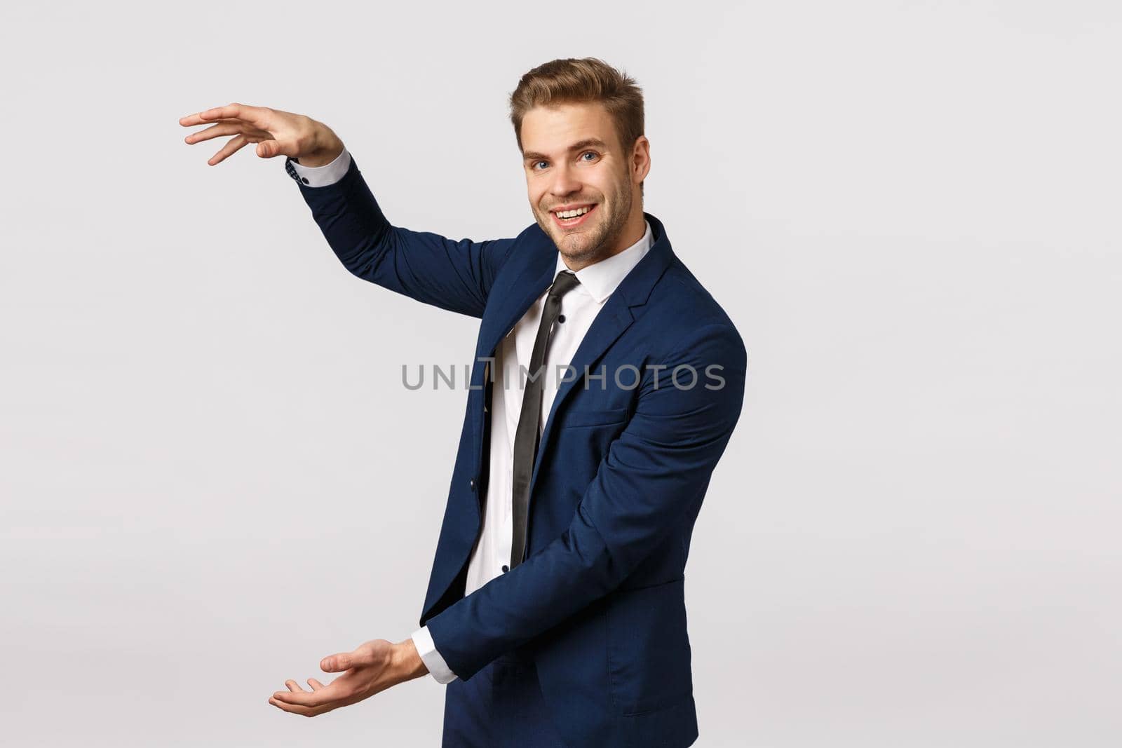 Cheerful charismatic young blond bearded male entrepreneur, wearing suit, discuss business, shaping big, large object over white background, smiling, introduce product, white background.