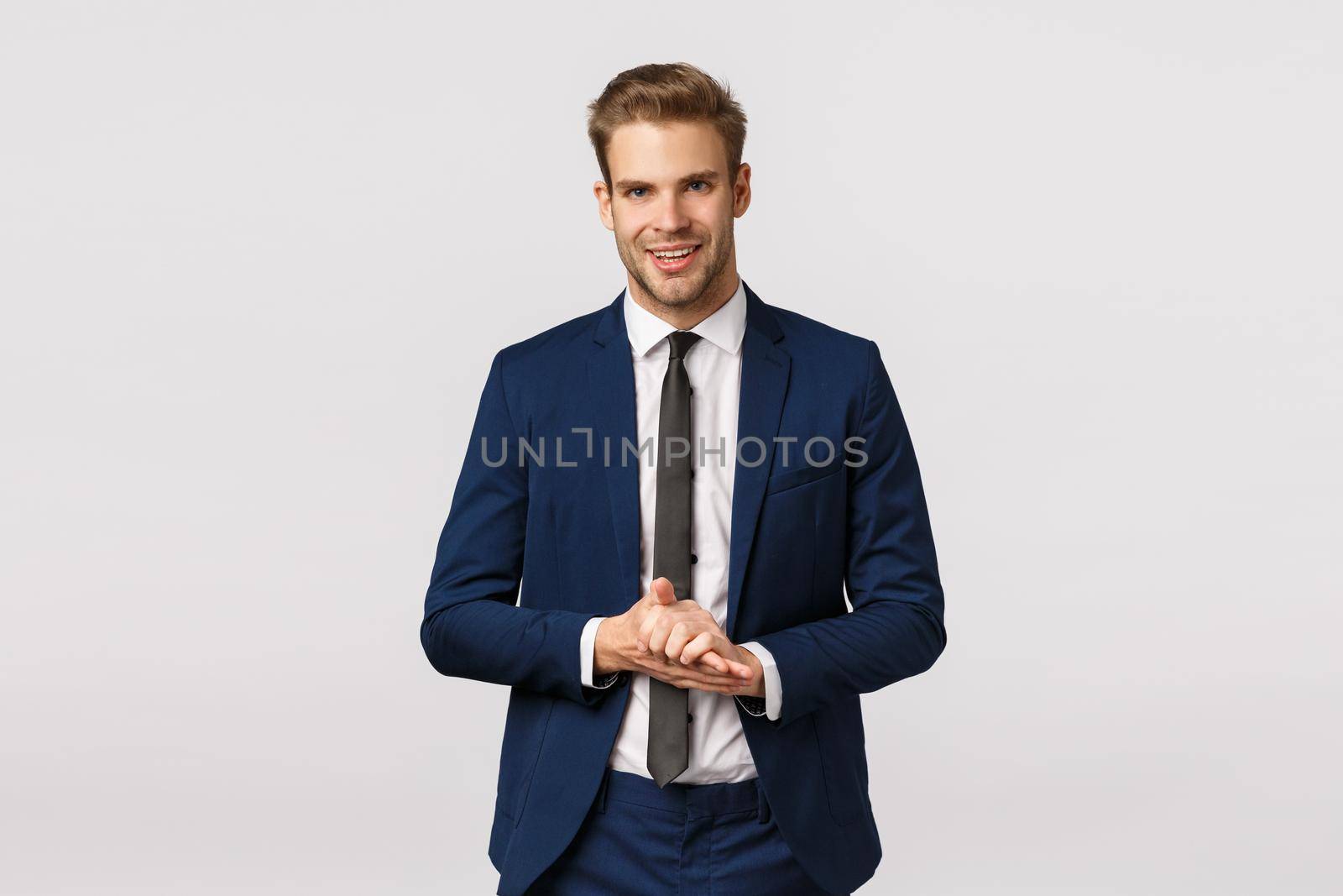 Handsome and confident, smart male entrepreneur in classic suit, rubbing palms and smiling pleased, anticipate make big money, good deal, relish something good, standing white background.