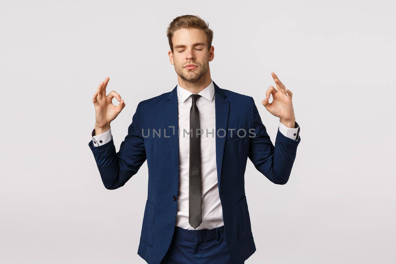 Dont panic, taking emotions under control. Peaceful and patient good-looking blond businessman in classic suit, make zen sign, spread hands sideways, close eyes, meditating, reliese stress.