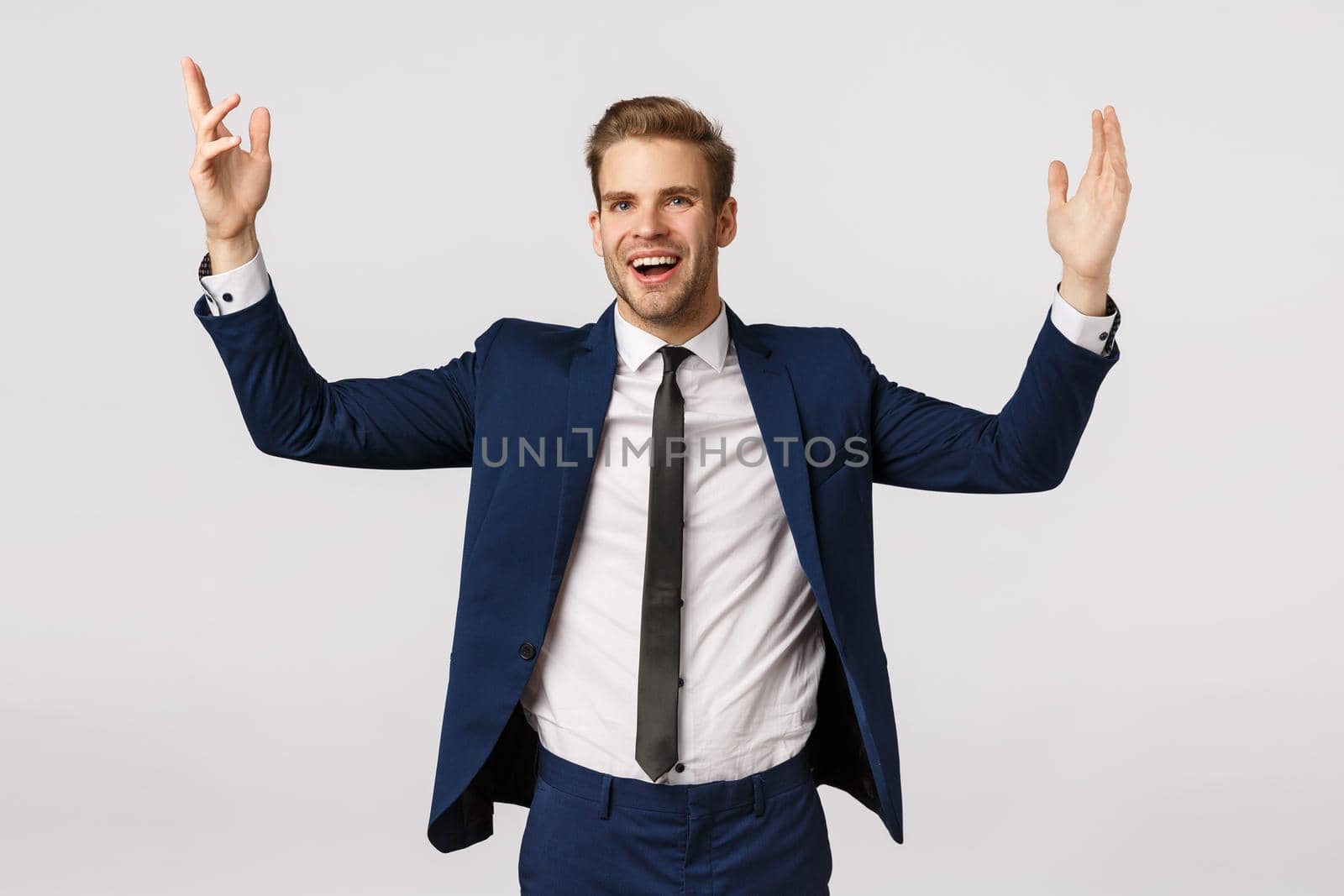Cheerful lucky and successful male entrepreneur in classic suit, raising hands up delighted, achieve goal, celebrating good deal, increased income, standing white background glad, feeling relieved.