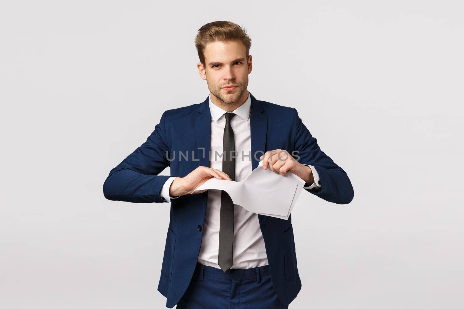 Guy fed up working, quit job. Displeased arrogant young snobbish businessman in classic suit, ripping documents, destroy report and smiling pissed, standing white background smirking.