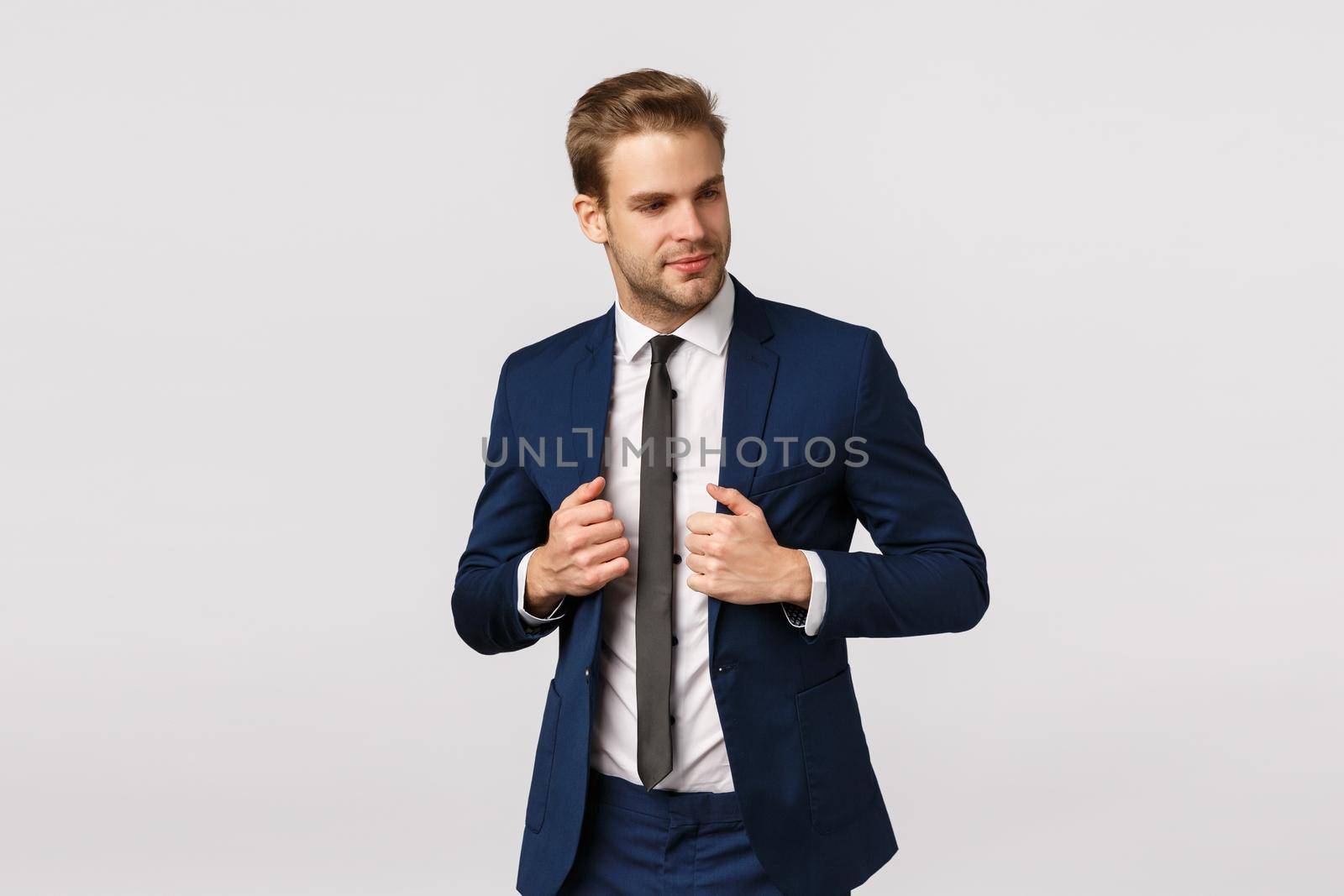 Success, confident and business concept. Attractive, handsome bearded blond guy in classic suit, adjusting jacket, looking at himself mirror, try new outfit for office meeting, white background.