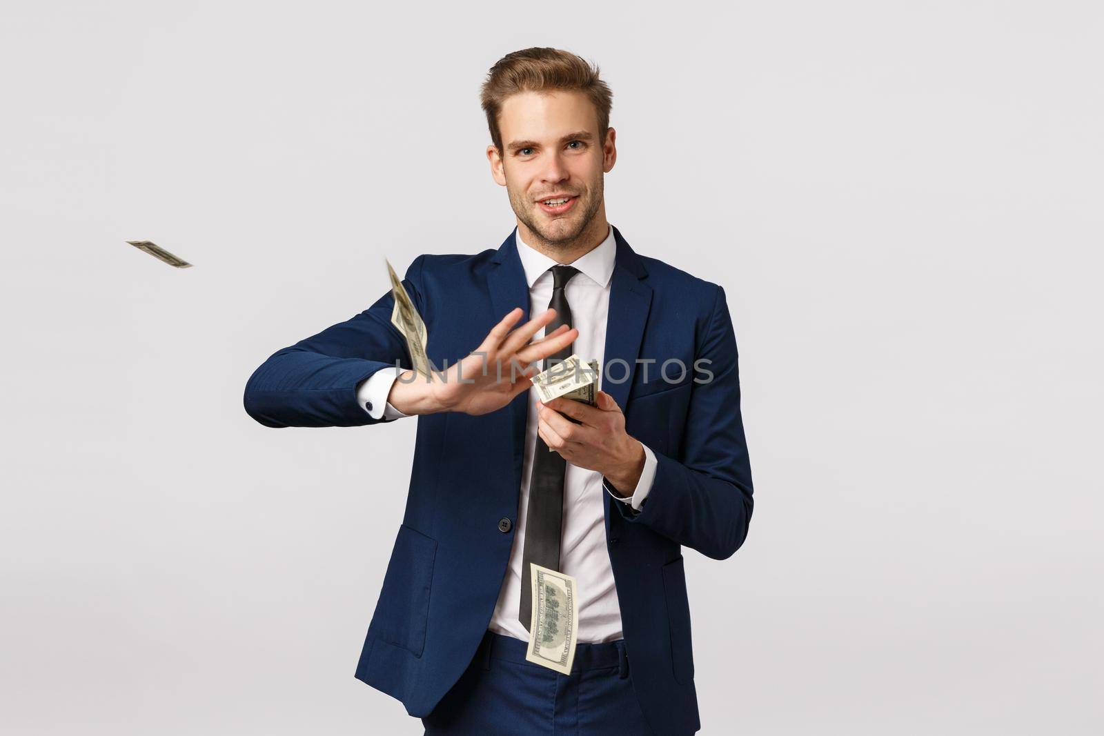 Success, money and finance concept. Handsome confident, blond bearded businessman in suit, holding cash and throwing money in air with pleased, satisfied expression, wasting dollars.