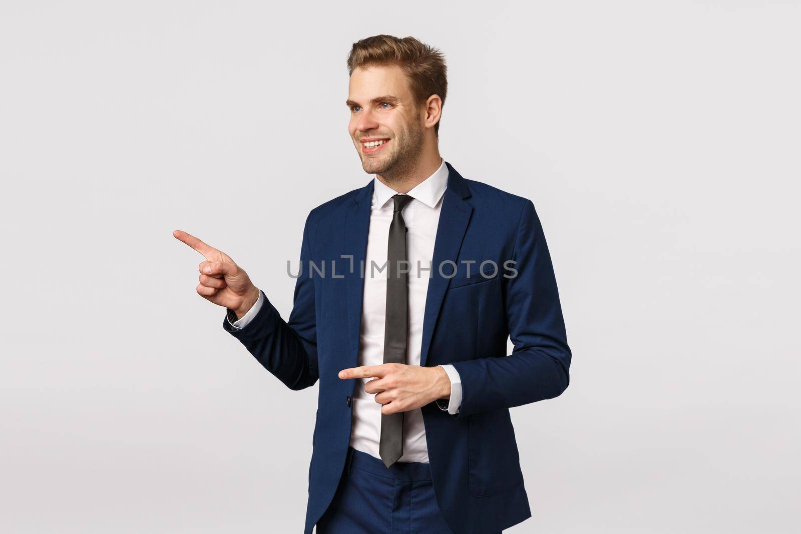Cheeky, confident rich and successful male entrepreneur, caucasian blond man in classic suit, pointing and looking left, smiling pleased, seeing wonderful product, exactly what looking for.