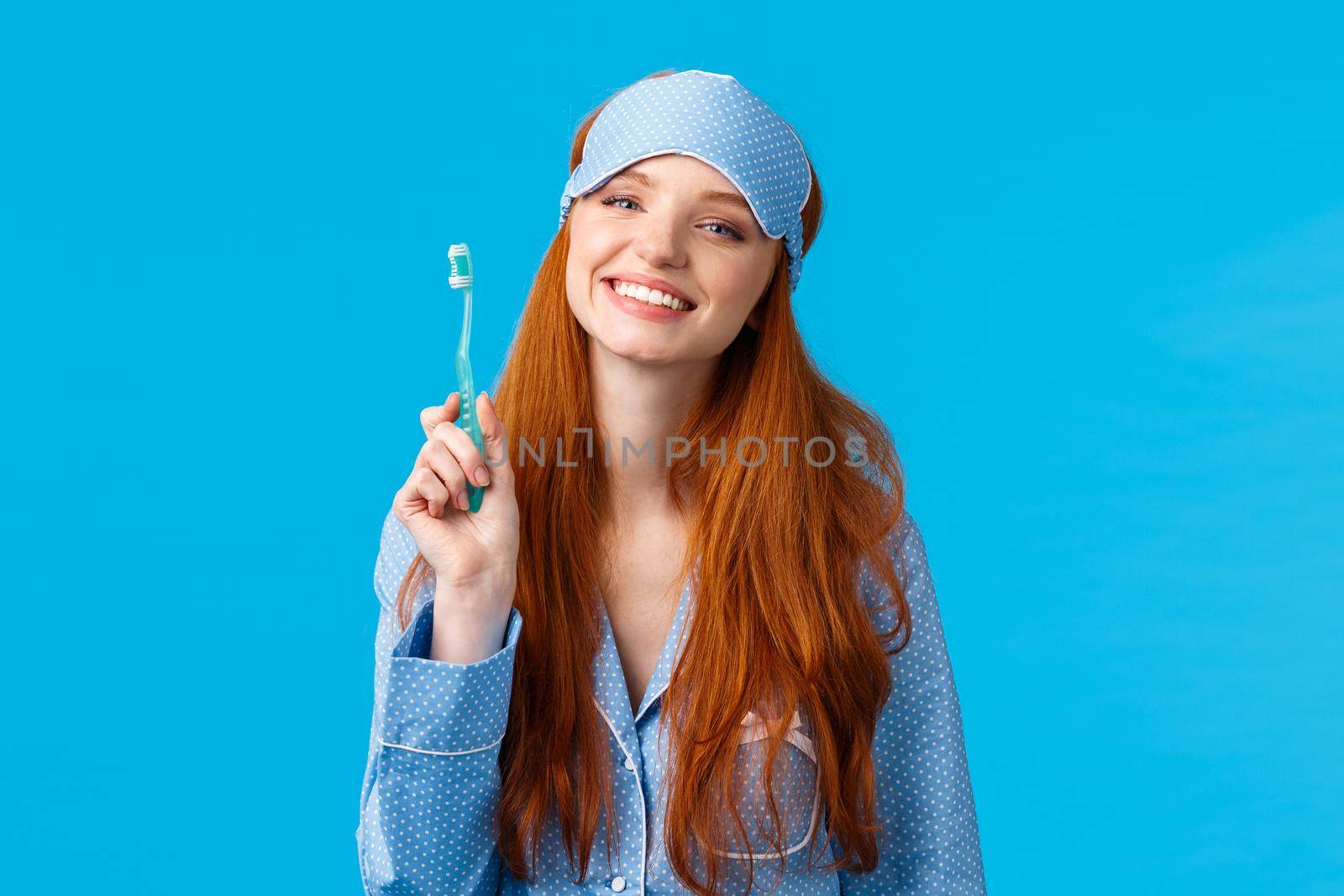 Health, lifestyle and beauty concept. Cheerful cute glamour redhead woman in nightwear and sleep mask, smiling happily, start morning brushing teeth and taking care personal hygiene.