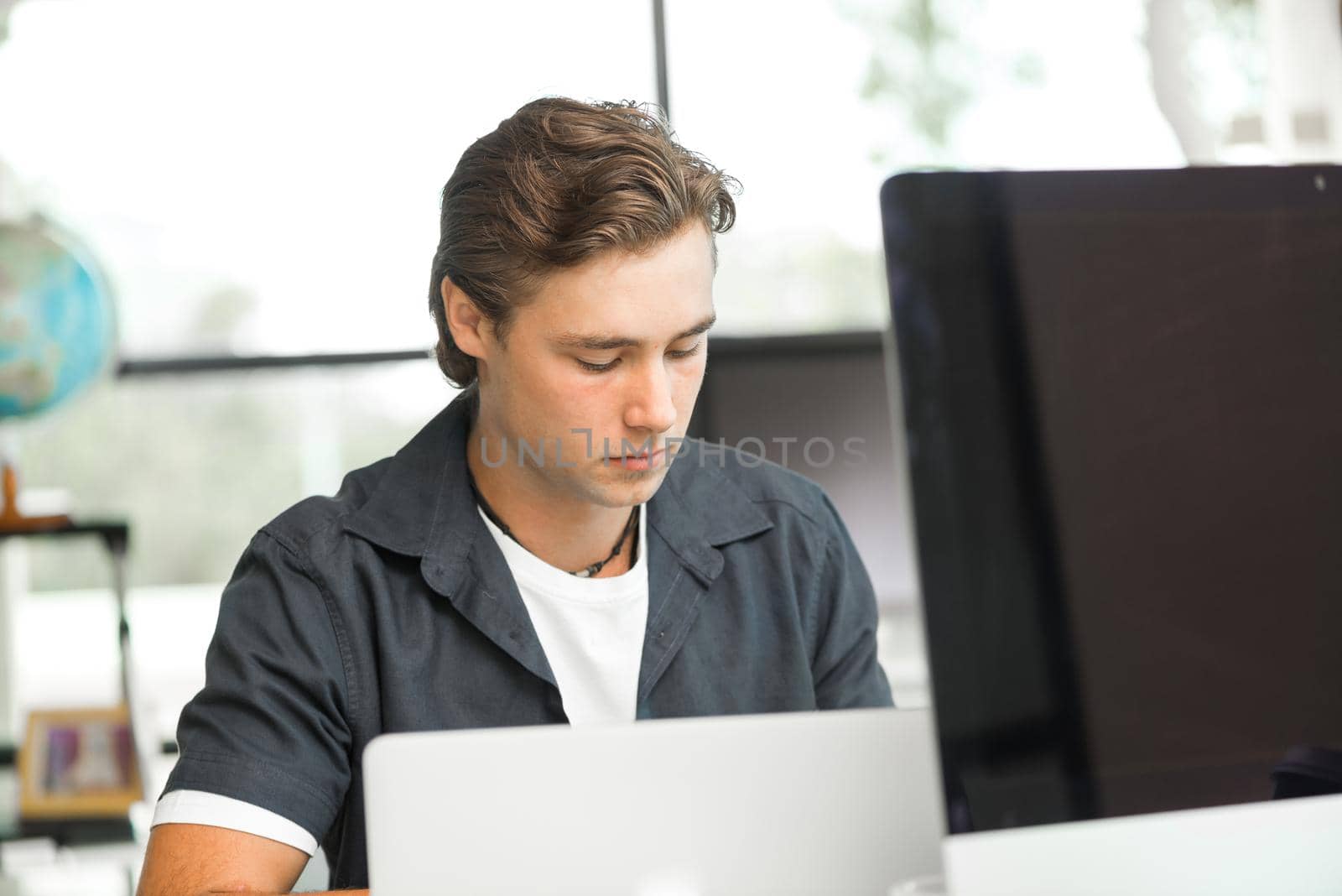 Young man in casual sitting at desk and working on computer