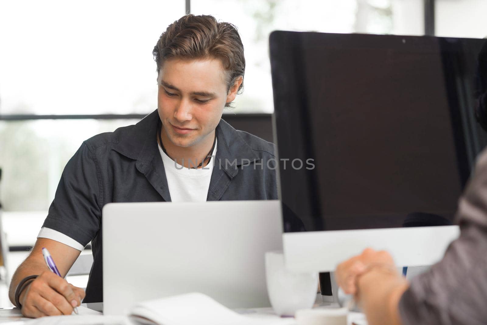 Young man in casual sitting at desk and working on computer