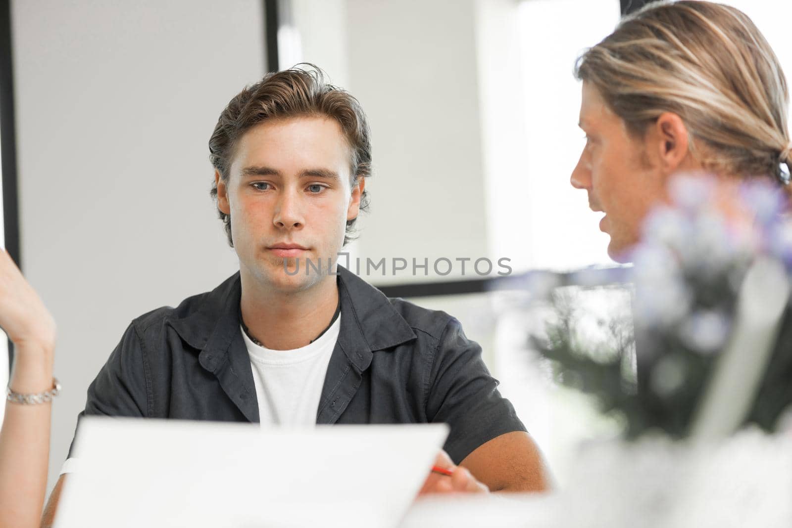 Young colleagues sitting at desk and having discussion in bright office