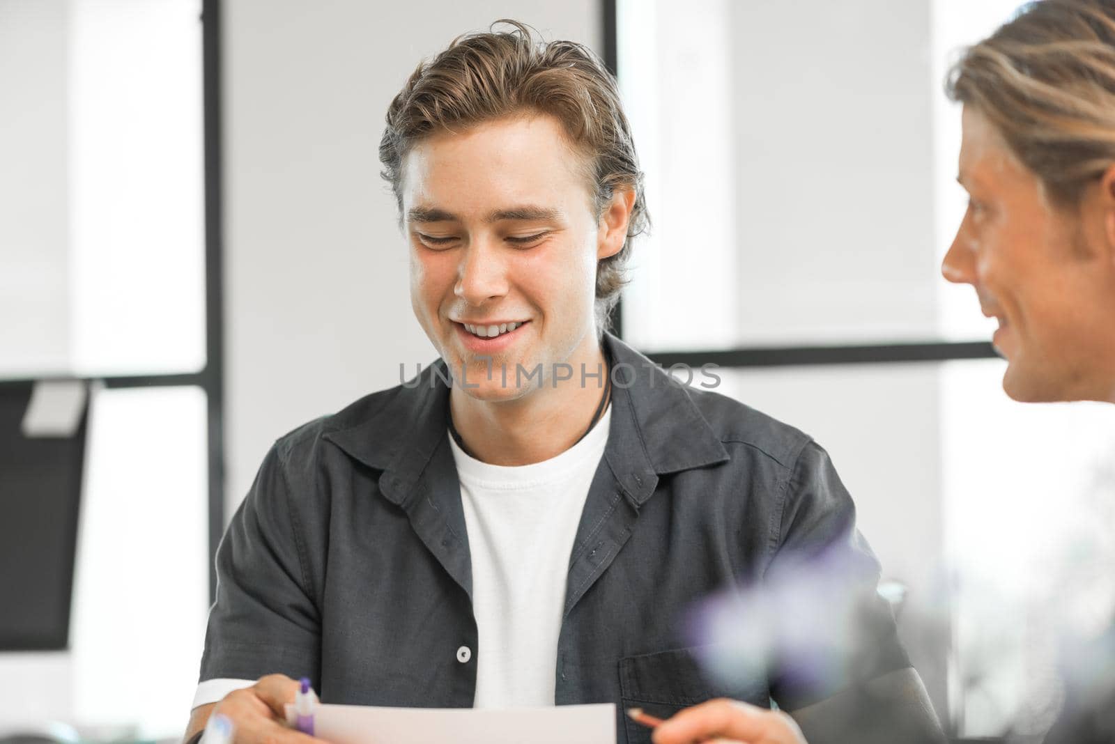 Young colleagues sitting at desk and having discussion in bright office