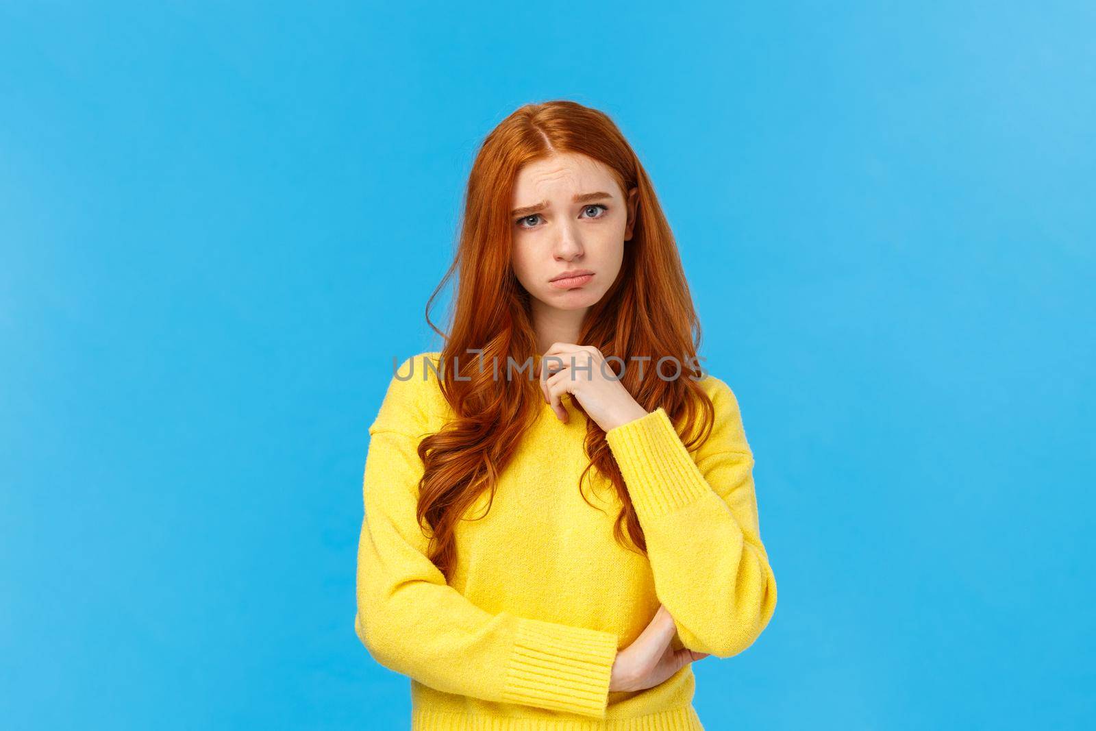 Upset redhead girl showing empathy, pity for friend hearing sad news, frowning and sulking feeling uneasy for person got in trouble, standing over blue background distressed or depressed.