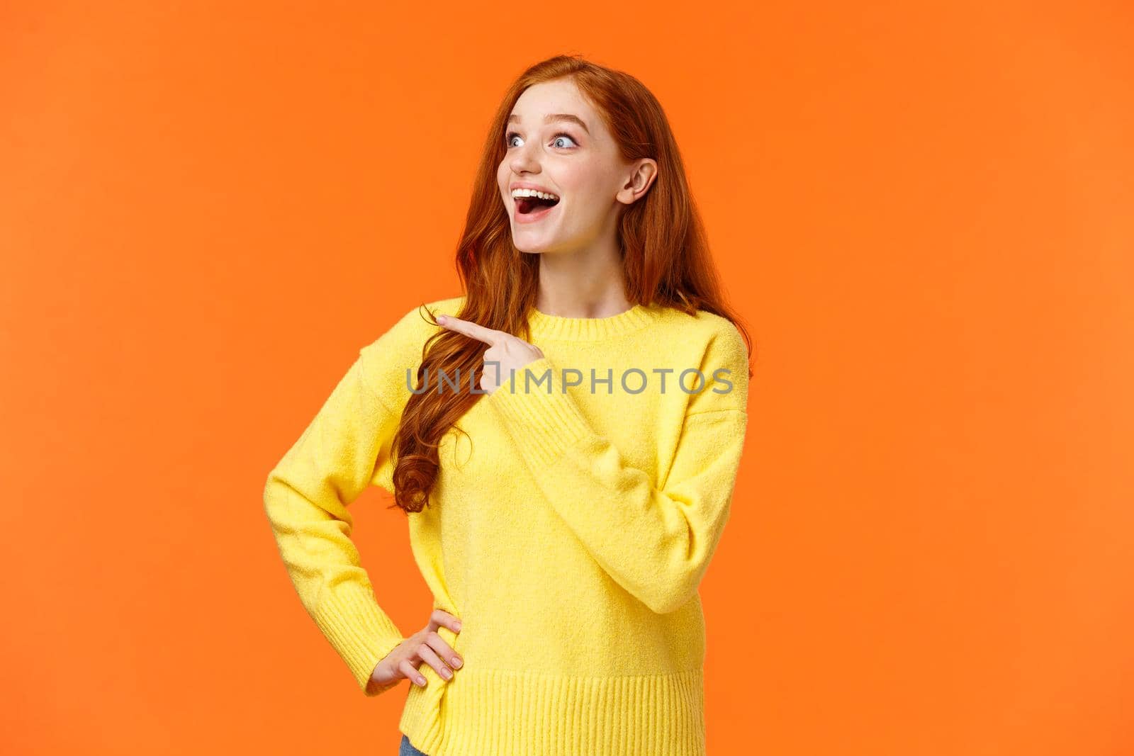 Look at that, wow. Impressed and fascinated, astonished cute redhead woman stare and pointing left with excited, happy smile, shoppaholic adore winter holiday sales, express interest and admiration.