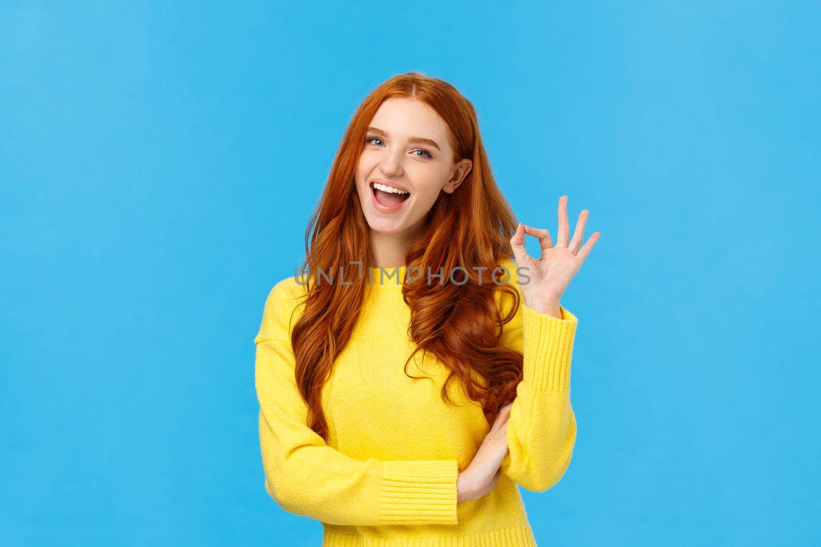 Waist-up shot carefree cheerful and friendly redhead gorgeous female freelancer finished IT school and showing okay gesture, no problem sign, smiling unbothered, assure all good, blue background.