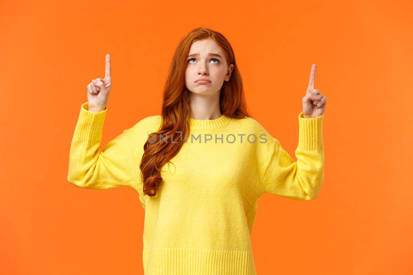 Sad and unhappy sulking redhead girl in yellow sweater, unsatisfied, look gloomy on christmas holidays, pointing and looking up envy or distressed, cant have desired gift, standing orange background.