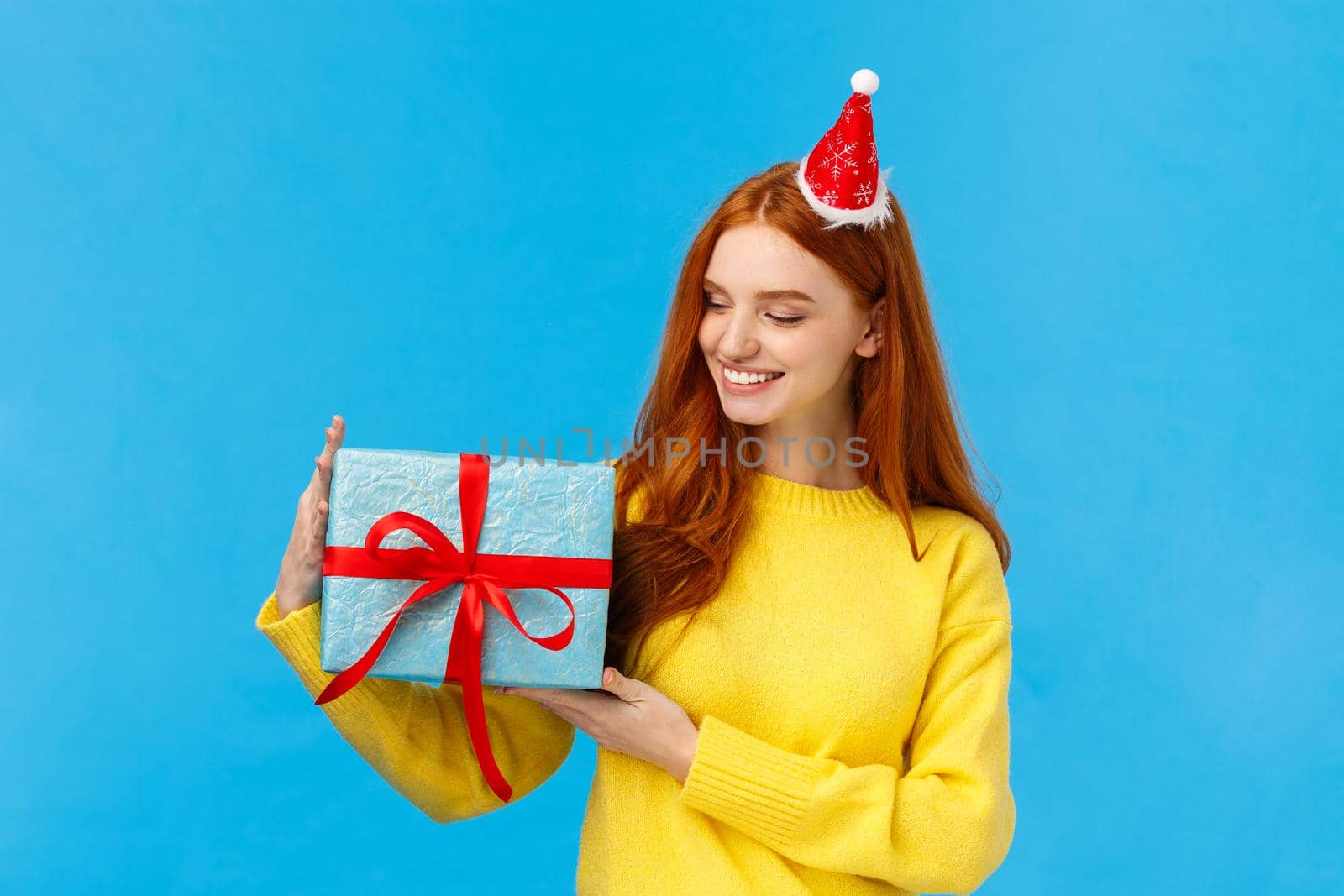 Holidays, love and family concept. Carefree tender and pretty redhead female holding cute wrapped box with gift, looking at present delighted, smiling happy, standing blue background joyful.